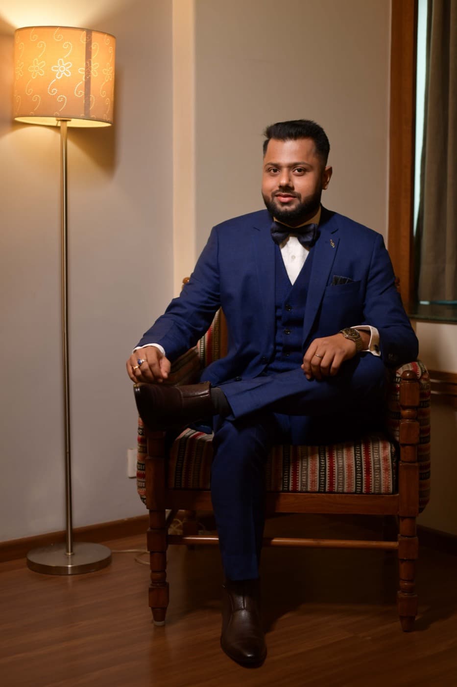 Groom seated in a chair beside a lamp for a styled portrait