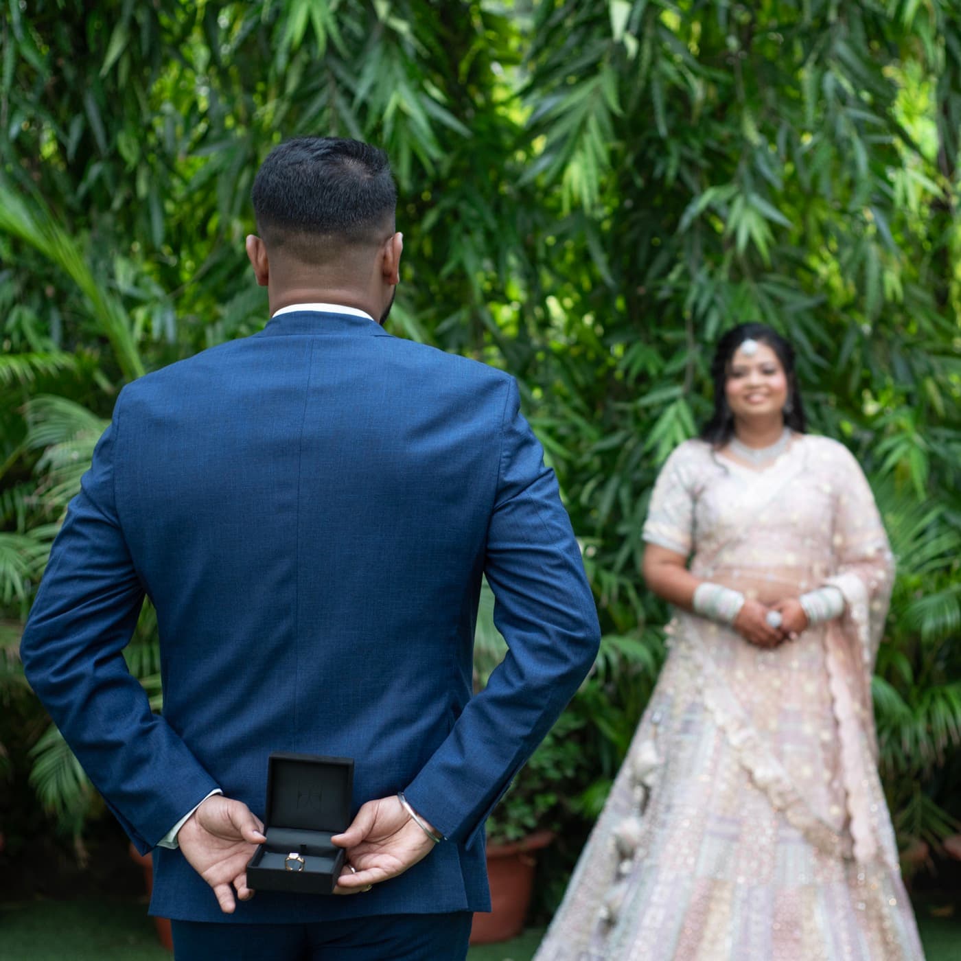 Groom holding a ring box behind his back as his partner approaches