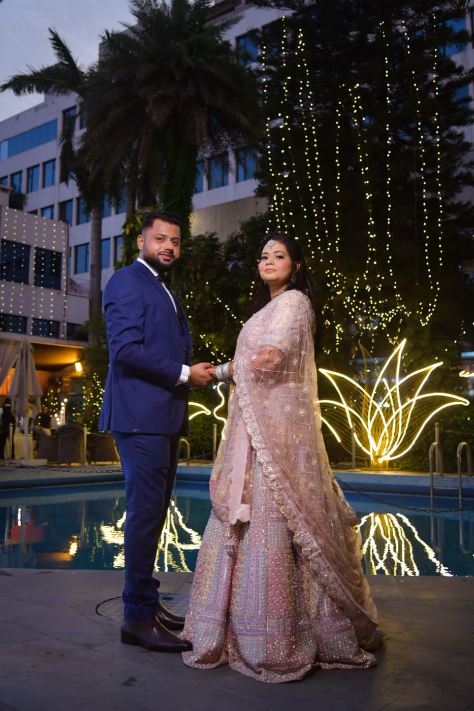 Couple holding hands beside a lit pool at night
